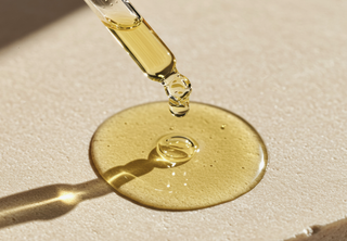 Tropfen Arganöl aus einer Pipette auf heller Oberfläche – Symbol für Anwendung und Pflegeroutine mit Arganöl