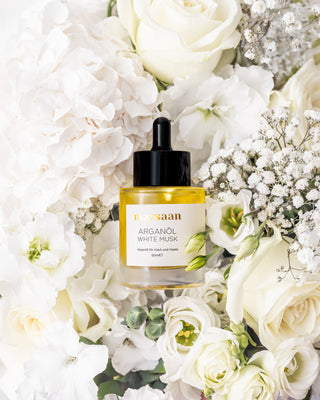 maysaan Arganöl White Musk – Flasche eingebettet in weiße Blüten, Flatlay-Aufnahme auf hellem Hintergrund. Pflegeöl aus Arganöl für Haut und Haare.